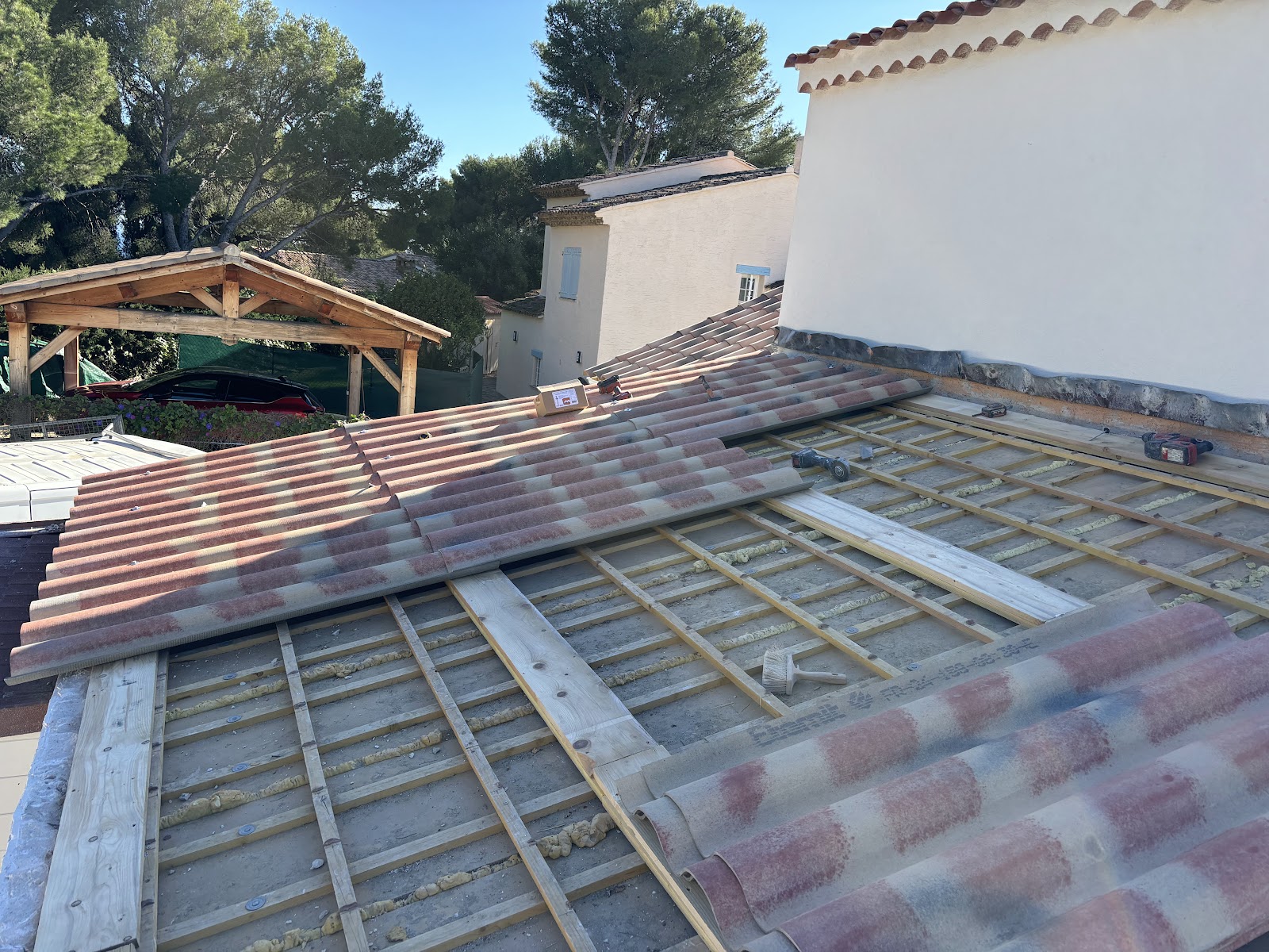 Charpente neuve avec tuiles rondes en cours de pose, carport en arrière-plan