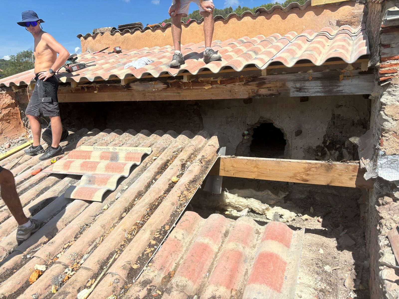 Toiture en rénovation : ancienne couverture ondulée partiellement déposée, nouvelle couverture en tuiles posée en partie haute