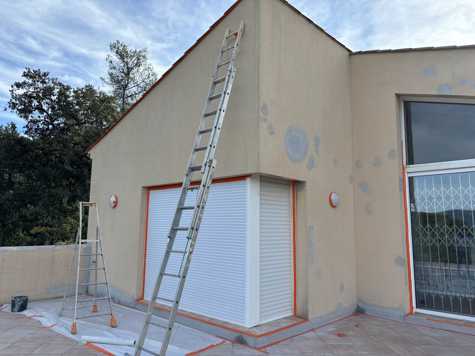 Façade avec taches d'apprêt grises, échelle et bâche de protection au sol