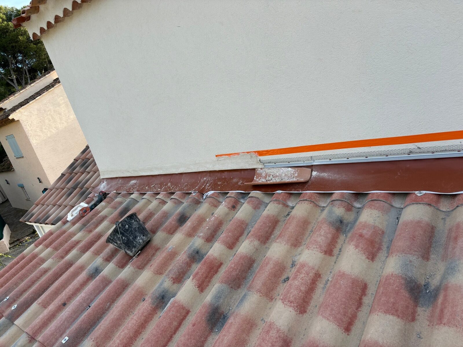 Pièce de zinguerie neuve posée au raccord entre la toiture et le mur, avec ruban de protection orange sur l'enduit